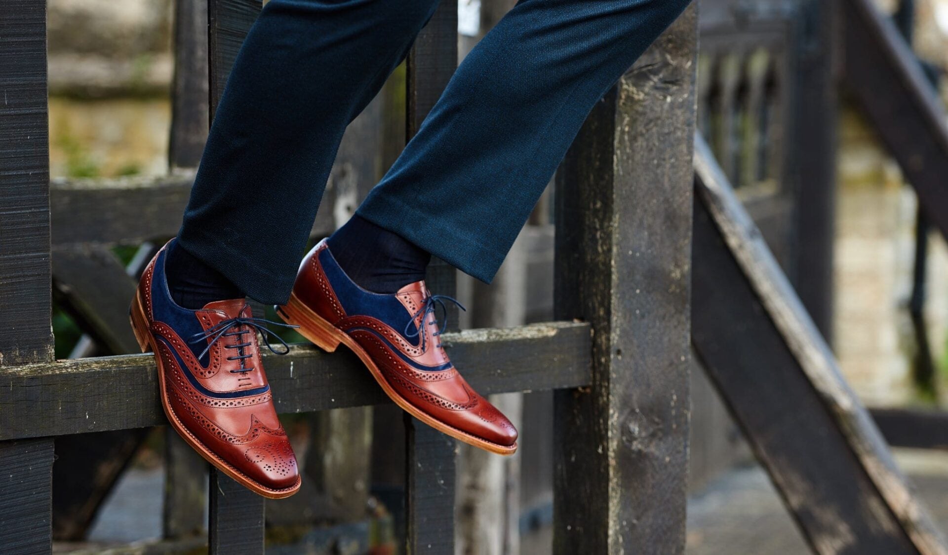Tan and burgundy brogues with navy suede heels worn over a black iron railing, photographed by Bell and Sons