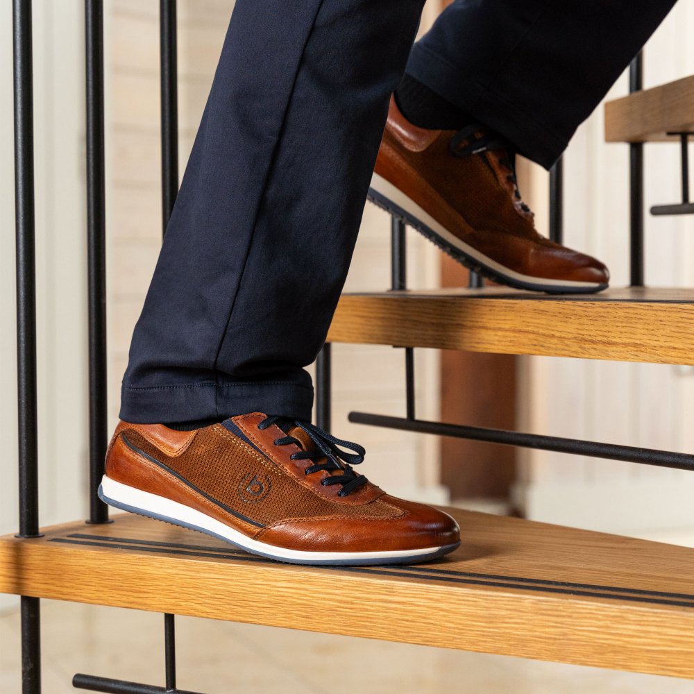 A tan Bugatti leather trainer on a wooden stair, paired with navy chinos, photographed by Bell and Sons
